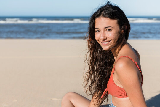 Smiling young woman sitting at beach during vacation