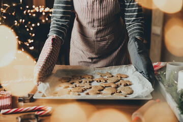 Merry Christmas, Happy New Year. Gingerbread cooking, cake or strudel baking. A young woman or mother holds deco, holding sheet with ready-made baked cookies in her gloves hands. High quality photo