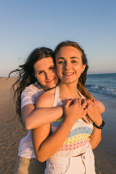 Smiling young woman embracing female friend at beach during sunset