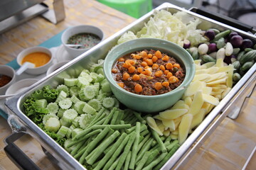 Thai food, Nam Prik Kai Poo (Crab’s Roe Chilli Dip) with many kinds of vegetables in buffet line. The container is a rectangular stainless steel tray. Selective focus.