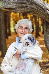 Beautiful Smiling Senior Woman Hugging her Havanese Dog in the Autumn Park