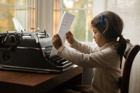 Little kid using typewriter and looking at paper