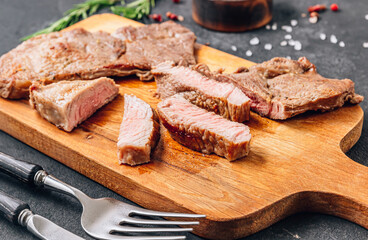 Fitness beef steaks with rosemary on wooden cutting board over black background.