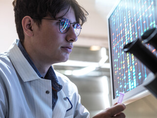 Male scientist with DNA sample examining test results in laboratory