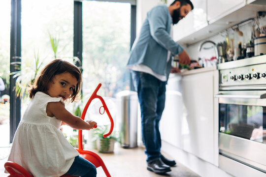 Girl sitting on rocking horse toy while father at kitchen counter