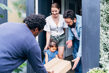 Parents helping daughter receiving package from delivery person at doorway