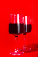 Valentine day gift box and wine glasses, with gold heart decor over red background copy space