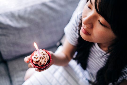 Young woman holding cupcake and candle while sitting on sofa