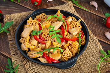 Tasty pasta in tomato sauce with chicken, pepper and herbs on wooden background