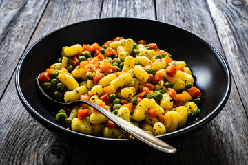Gnocchi with green peas and carrots on wooden table
