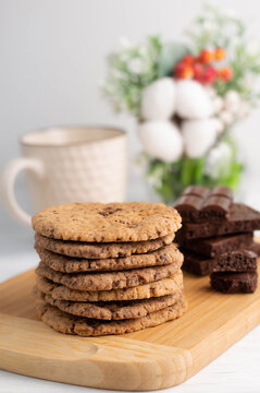 Blurred foreground image of giant chocolate chip cookies on a board, chocolate pieces and a cup of tea.