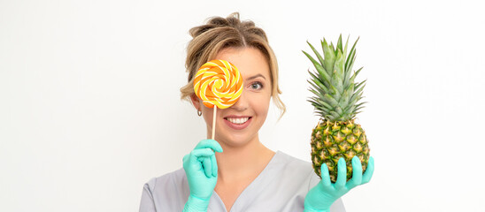 Beautiful smiling beautician holding fresh pineapple and cover her eye with lollipop over white background. Skincare cleansing eco organic