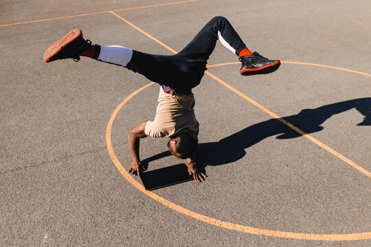 Young man balancing with handstand using graphics tablet on basketball court during sunny day
