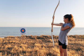 Archeress aiming at target while standing on grass during sunny day