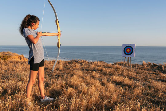 Young woman practicing archery while standing on grass at beach