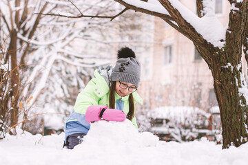 Little girl having fun in snowy yard. Happy kid playing with snow