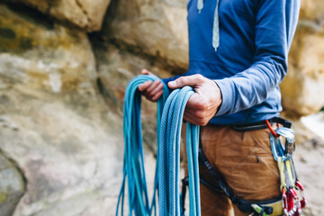 Close-up of a strong climber with equipment on a belt holding rope and preparing to climb