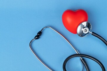 Stethoscope and rubber red heart on a blue background with space for text. Heart health, healthcare concept. Flat lay