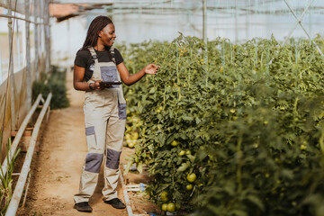 Smiling female farmer holding string supporting plants at greenhouse