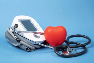 Stethoscope, blood pressure monitor and rubber heart on a blue background with space for text. Heart health, healthcare concept.