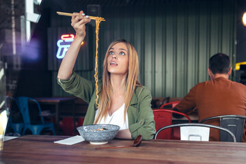 Funny beautiful woman eating ramen with chopsticks in asian restaurant.