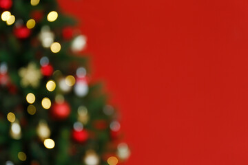 Blurred out decorated Christmas tree in soft yellow lights with bokeh effect over isolated red...