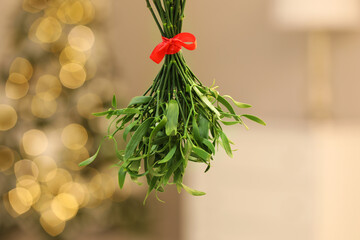 Mistletoe bunch with red bow on blurred background, bokeh effect. Traditional Christmas decor