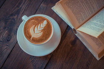 Cup with ready-made coffee on a wooden background with an open book. view from above. Selective focus.