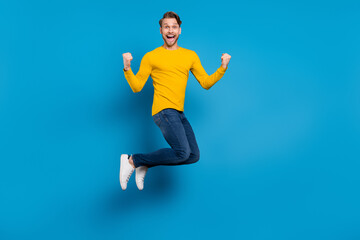 Fototapeta na wymiar Full length body size of young guy smiling jumping up gesturing like winner isolated bright blue color background