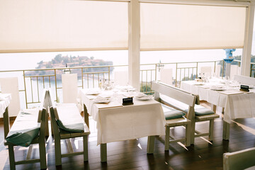 Restaurant with long benches and tables covered with tablecloths overlooking Sveti Stefan island 