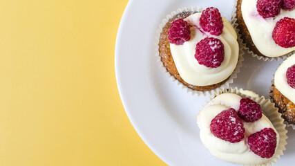 Homemade cupcakes with white cream and berries on a yellow background of flats.