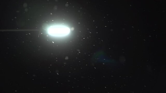 Lonely street light with color light leak in night when windy and snowing. Snowing with different speed from left to right. Light will turn off in the end.