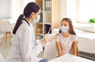 Happy little kid wearing a mouth covering getting a shot at a modern clinic. Friendly nurse or...