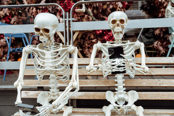 Halloween decoration near cafe or restaurant, modern skeletons sitting, talking, using mobile...