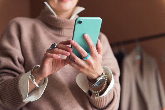 cropped picture fashion woman in brown oversize sweater and trousers standing in modern work place or office with smartphone