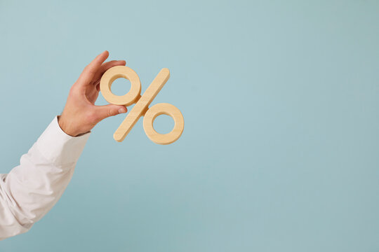 Human hand holding percent symbol. Entrepreneur or client holding percentage sign on blank blue color text copyspace background. Business, finance, mortgage rates, value added tax, or discount concept