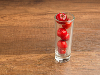 Close-up of red acerola cherries in a glass on a wooden table. High vitamin C and antioxidant fruits