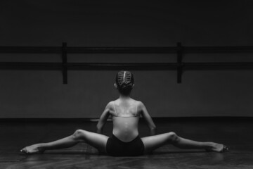 Panoramic black and white view of a beautiful young ballerina doing the splits, stretching her legs in a pose on stage, in the studio. Elegant performer, flexibility of concept, strength discipline