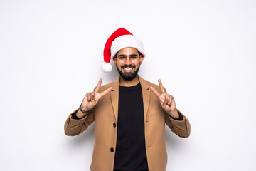 Fototapeta na wymiar Young handsome man wearing a Santa hat over white background doing peace symbol with fingers over face, smiling cheerful showing victory