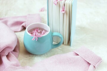 Obraz na płótnie Canvas Cup with a drink, fresh flowers bookmarks in an open book, woolen pink sweater on a light background, top view, romantic congratulation, love emotion