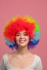 Portrait of woman with rainbow curly hairstyle. Smiling young attractive female in colorful wig on pink background. Close-up.