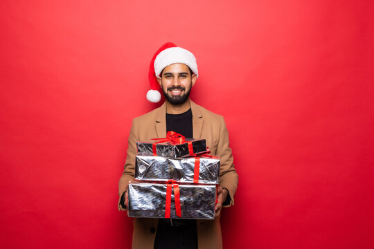 Handsome romantic guy is looking at camera and smiling while holding a present for his couple, on red background