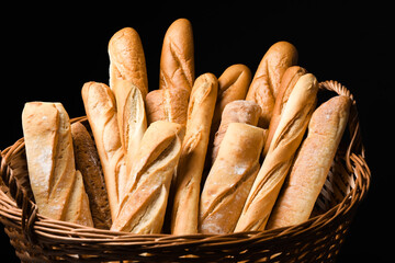 Fresh tasty baguettes in basket against black background, closeup