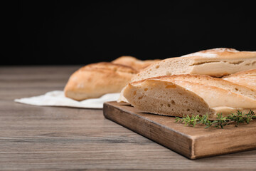Cut tasty baguette with thyme on wooden table. Space for text