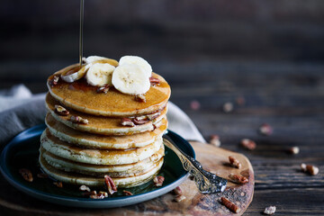 Maple syrup pouring onto pancakes served with fresh banana fruit and nuts. Selective focus with...