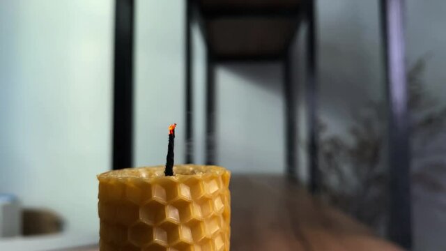 Blowing out burning decorative candle made of natural textured beeswax with honeycombs on table in craft workshop close view