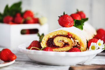 Homemade strawberry shortcake cake roll or Roulade with a berry jam filling and powdered sugar with mint leaves. Dessert over a white rustic wooden table. Selective focus with blurred foreground and b