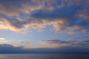 Naklejka na ściany i meble 明け方の冬の海。太陽が昇り雲の間から顔を出し、水面はキラキラと輝く。兵庫県芦屋市芦屋浜で撮影。