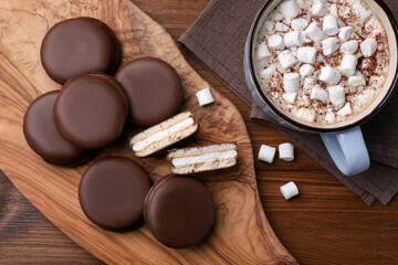 Fototapeta na wymiar Tasty choco pies and cocoa with marshmallows on wooden table, flat lay