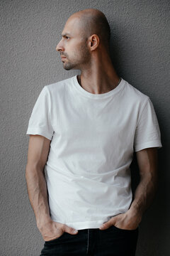 Image of a handsome bald man in a white T-shirt on a gray background